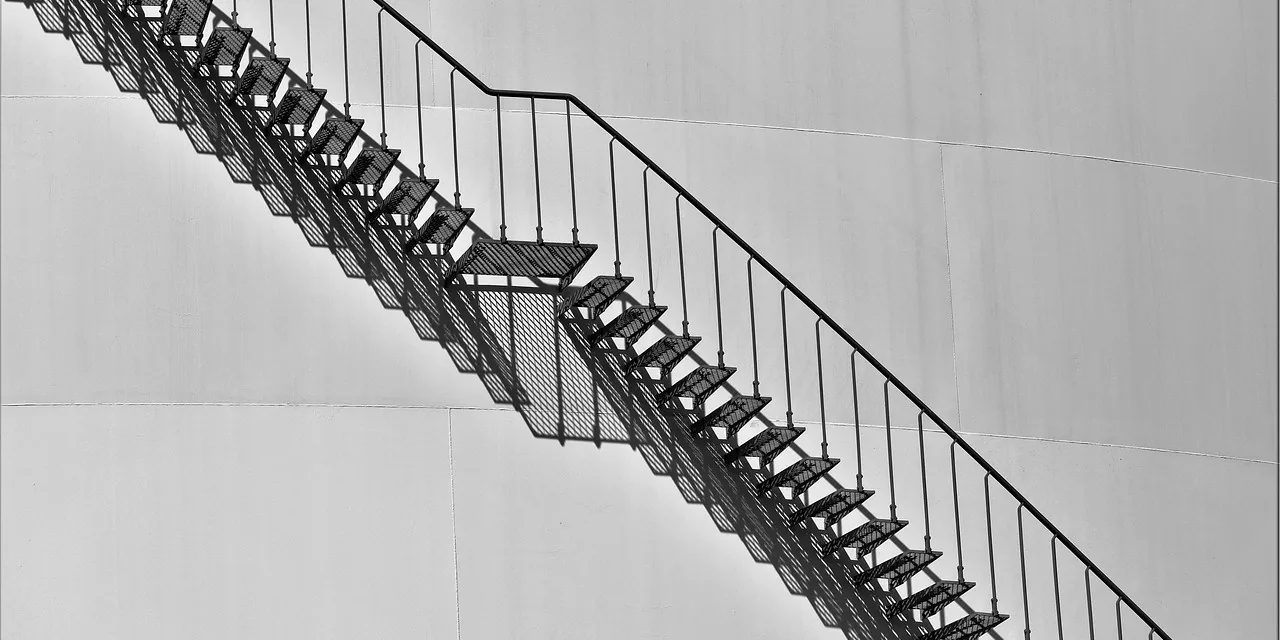 Escalier métallique extérieur plaqué contre un grand mur de béton clair, sans personne dessus